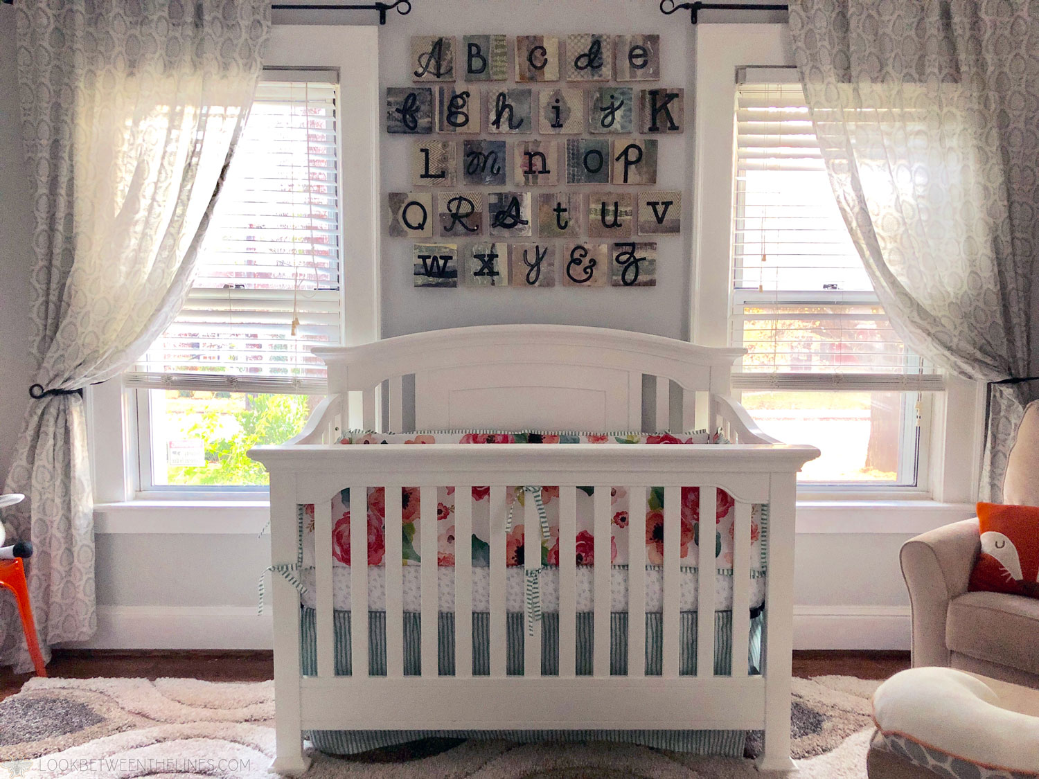 Baby girl's crib with a floral pattern bumper, bright windows, and the ABC's hanging on the wall.